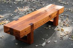 a wooden bench sitting on top of a cement ground next to leaves and fallen leaves