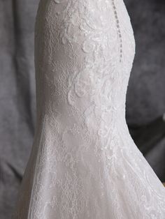 the back of a wedding dress on display in front of a gray background with white flowers