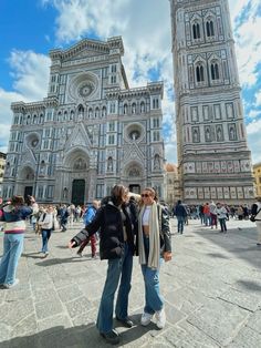 two people standing in front of a large building with towers on each side and blue sky behind them