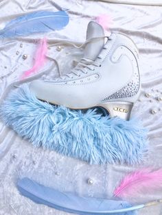 a pair of white ice skates with blue feathers around them on a bed sheet