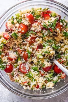 a glass bowl filled with couscouse and topped with tomatoes, broccoli