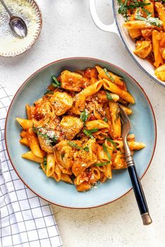 pasta with chicken and sauce in a bowl next to a serving dish on a table