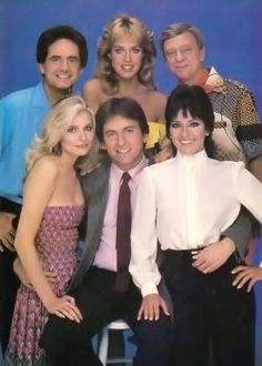 a group of people standing next to each other in front of a blue background with one man wearing a white shirt and tie