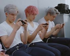 three young men sitting next to each other holding cell phones