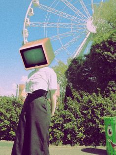 a person standing in front of a ferris wheel with an old tv on their head