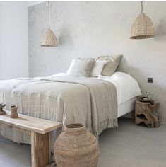 a bedroom with white walls and flooring, two hanging lights above the headboard