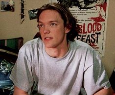 a young man sitting on top of a bed next to a wall with blood all over it