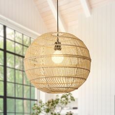 a light fixture hanging from the ceiling in a room with large windows and wooden flooring