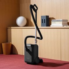 a black vacuum sitting on top of a red carpet next to a wooden shelf with books