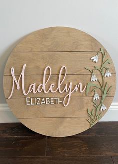 a wooden sign that says madelyn elizabeth with flowers and leaves painted on the front