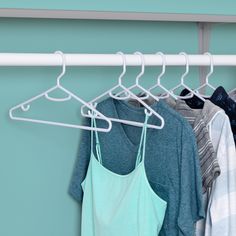 three shirts hanging on a clothes rack in front of a blue wall with white hangers