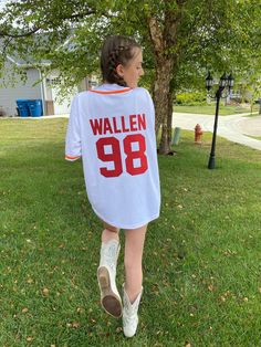 a woman walking in the grass wearing a white shirt that says wallen 98 on it