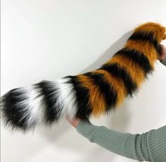 a person is holding a cat tail in their hand and it looks like the tail has been painted black, white, and orange