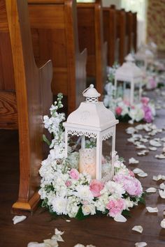 a white lantern surrounded by flowers and petals on the ground at a wedding ceremony in an old church