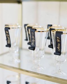 wine glasses are lined up on a shelf with black ribbon and name tags attached to them