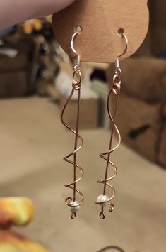 a pair of silver earrings hanging from a hook on a piece of wood next to a chair