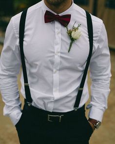 a man wearing a white shirt and black suspenders with a flower in his lapel