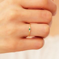 a woman's hand wearing a gold ring with an emerald stone