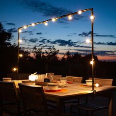 an outdoor dining table with lights strung over it at night, in front of the sky