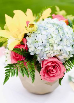 a vase filled with lots of flowers on top of a white table covered in greenery