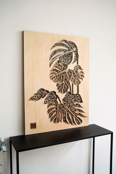 a wooden wall hanging on the side of a white wall next to a black shelf