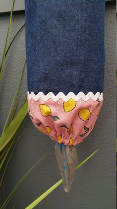 a blue bag with yellow lemons on it is hanging from a plant in front of a gray wall