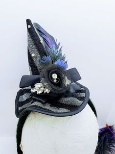 This Witch Hat Fascinator is an easy and classy way to dress up this year! This is a black and silver witch hat that is attached to a black yarn wrapped headband. The hat is adorned with ruffled lace, a netted flower, rhinestones and iridescent feathers. Will Fit a 4 year old and up! Like our Facebook Page and get 10% off when you message me before checkout! Everything made by handmade MKE is one of a kind and unique, however, if you would like a different size or see a piece that you would like Curved Brim Costume Hats And Headpieces, Novelty Brimmed Costume Accessories For Party, Witchy Winter Party Costume Hats And Headpieces, Fitted Costume Accessories For Carnival And Halloween, Fitted Top Hat For Halloween Costume, Curved Brim Halloween Costume Hats And Headpieces, Curved Brim Costume Hats And Headpieces For Halloween Party, Adjustable Curved Brim Costume Accessories For Halloween, Black Top Hat For Halloween Party