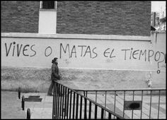 black and white photograph of a man walking down the street in front of a wall with writing on it