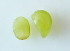 two pieces of green fruit sitting next to each other on a white surface with one piece cut in half