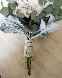 a bouquet of white flowers and greenery tied to a wooden table with leaves on it