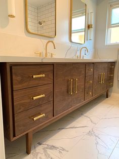 a bathroom with marble counter tops and gold handles on the sink cabinet, along with two mirrors