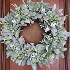 a wreath with white flowers and greenery is hanging on a wooden door, ready to be hung