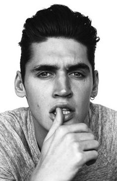 a black and white photo of a young man with his finger in his mouth looking at the camera