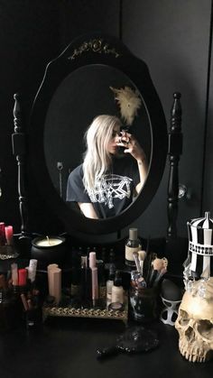 a woman taking a selfie in front of a mirror with candles and skulls on the table