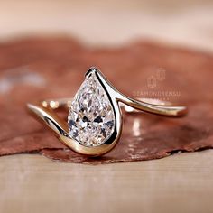 a pear shaped diamond ring sitting on top of a leaf