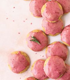 pink frosted cookies with rosemary sprig on top are arranged on a white surface