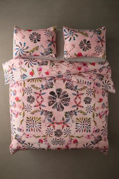 a bed with pink and blue flowers on it's comforter, next to two pillows