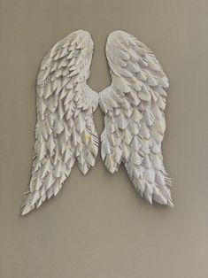 two white angel wings made out of paper on a gray surface with one wing folded back to the other side