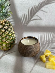 a pineapple next to a candle and sliced pineapples on a white surface