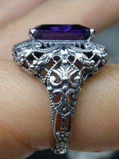 Purple Amethyst CZ (Cubic Zirconia) Sterling Silver RingIntricate Design#D149 This is a beautiful Victorian era reproduction ring. The sterling silver filigree holds a ~6-carat gemstone. The gemstone has perfect color and amazing clarity. The flawless high-quality rectangle-cut gemstone is 12mm x 10mm. The ring is 3/4" North to South on the finger. The inside of the band is marked 925 for sterling silver. Notice the intricate and dramatic detail of the floral silver filigree setting in this Vict Victorian Style Purple Amethyst Ring For Gift, Victorian Sterling Silver Rings With Purple Stone, Luxury Victorian Amethyst Ring In Purple, Victorian Silver Amethyst Ring, Victorian Style Hallmarked Amethyst Ring, Purple Love, Cubic Zirconia Rings, Sterling Silver Filigree, Cz Ring