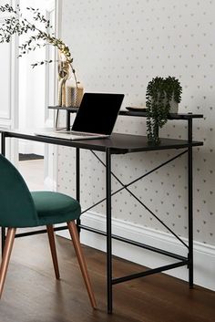 a laptop computer sitting on top of a desk next to a green chair and potted plant