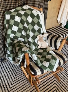 a green and white blanket sitting on top of a rocking chair next to a window