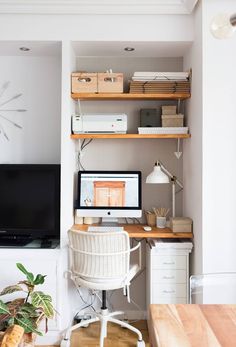 a desk with a computer on top of it in front of a wall mounted tv