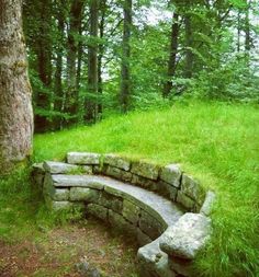 a stone bench sitting in the middle of a lush green field next to a tree