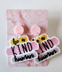 two pink and yellow earrings with the words be a kind of kind of human on them