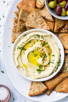 hummus with olives and pita chips on a white platter, ready to be served