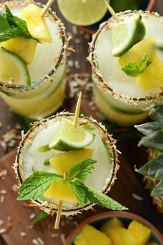 three margaritas with lime and mint garnish on a wooden table next to other drinks