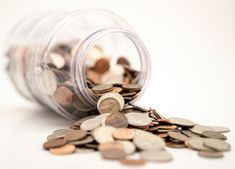 a glass jar filled with coins on top of a white table next to a pile of pennets