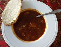 a white plate topped with soup next to a piece of bread on top of a table