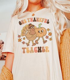 "Get ready to show your gratitude this Thanksgiving with our \"One Thankful Teacher\" t-shirt!  Whether you're celebrating the holiday with your little learners or simply spreading a message of thankfulness, this shirt is a must-have for any teacher.  DETAILS * Bella + Canvas Unisex Premium T-Shirt  * Soft and lightweight  * 100% combed and ring-spun cotton  * Athletic Heather is 90% combed and ring-spun cotton, 10% polyester * Design is printed using DTG technology which uses high-quality water Fun Custom Print T-shirt For Teacher Appreciation, Funny Long Sleeve T-shirt With Custom Print, Thanksgiving Graphic Print Crew Neck T-shirt, Pre-shrunk Long Sleeve T-shirt As A Gift, Long Sleeve Screen Print T-shirt As Gift, Long Sleeve Pre-shrunk T-shirt As Gift, Long Sleeve Screen Print T-shirt Gift, Fun Long Sleeve T-shirt With Custom Print, Long Sleeve Fun T-shirt With Custom Print